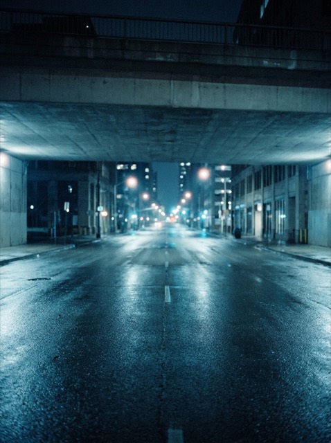 A rain slicked street at night under cool blue streetlight